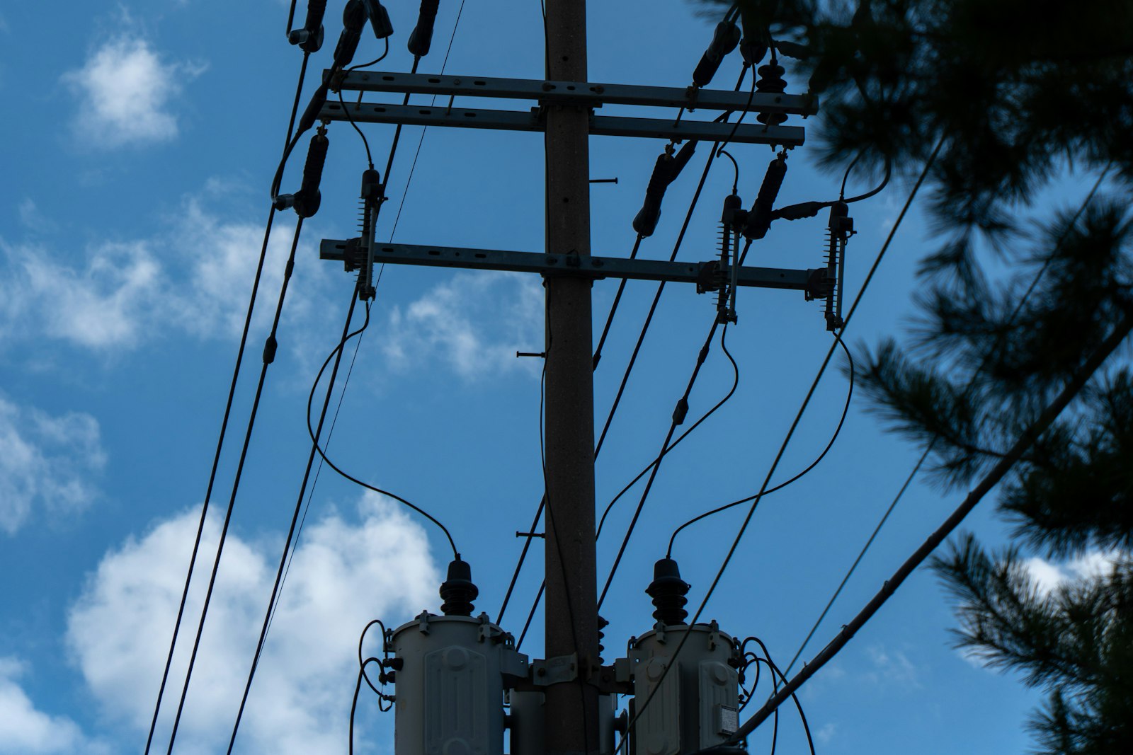 Distribution pole with transformers and feeder lines against a blue sky